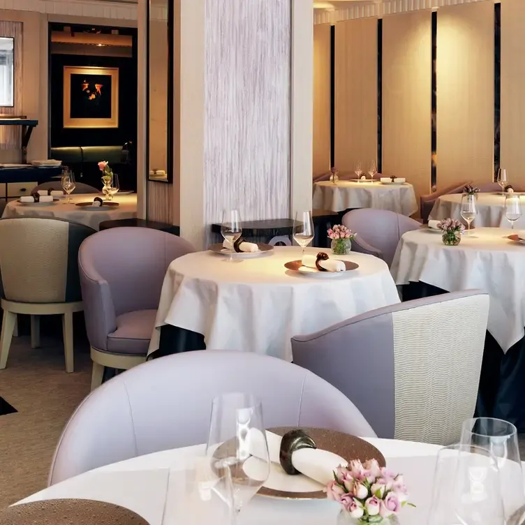 The interior of Restaurant Gordon Ramsay with round tables topped with white tablecloths surrounded by purple and white armchairs.