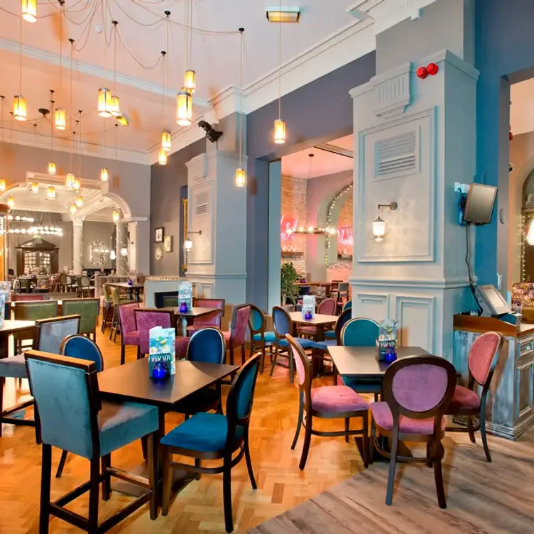 The wooden floor, blue and purple velvet chairs, and light blue walls of the dining room at Slug and Lettuce.