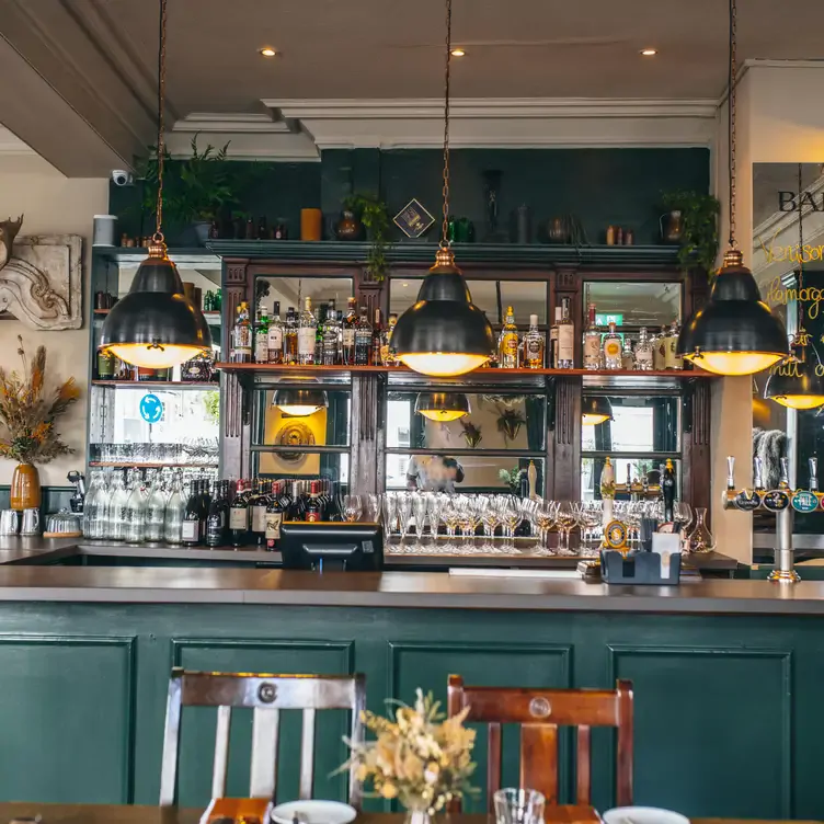 The forest-green bar at Harwood Arms with bottles of wine and spirits lining the shelves and warm lights hanging from the ceiling.