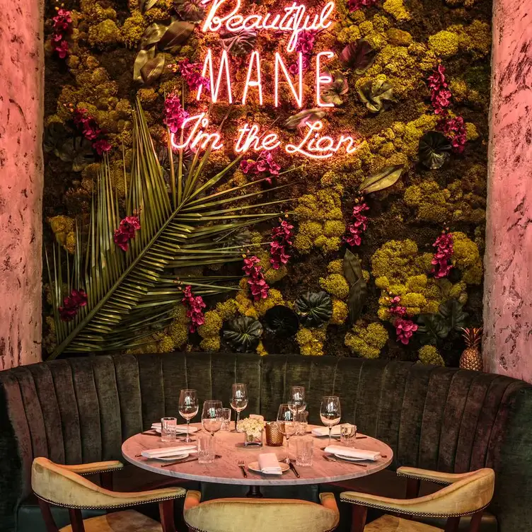 A table and round seating with pink lighting and plants on the wall at Menagerie Restaurant, one of the best bottomless brunch restaurants in Manchester.