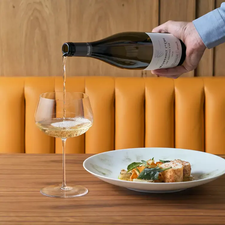 A waiter pours white wine into a glass that sits next to a dish at Trivet in London