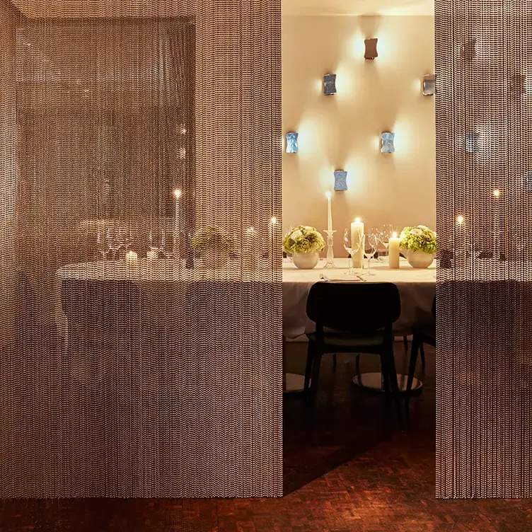 A table partially obscured by a shimmering beaded curtain. It is set with glowing candles, cutlery, glasses and flowers.