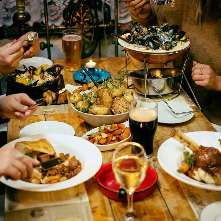 Diners sit around a wooden table eating dishes of lamb, mussels and potatoes.