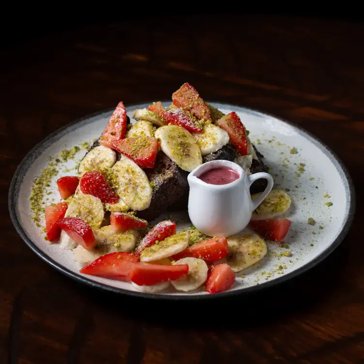 A dish of banana bread topped with strawberries and bananas with a side of sauce at Greenwoods, one of the best brunch restaurants in Edinburgh.