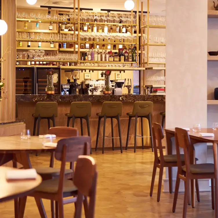 Bright interiors with wood furniture and a large bar with bottles lined up on the walls at Trivet in London