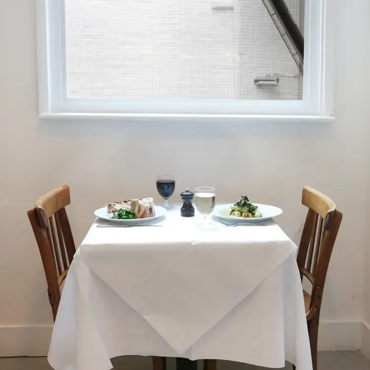 A table for two laid with dishes and drinks in front of a window at St JOHN Smithfield, one of the best MICHELIN Star restaurants in London