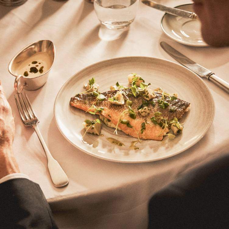 A diner sits at table with a fish dish.