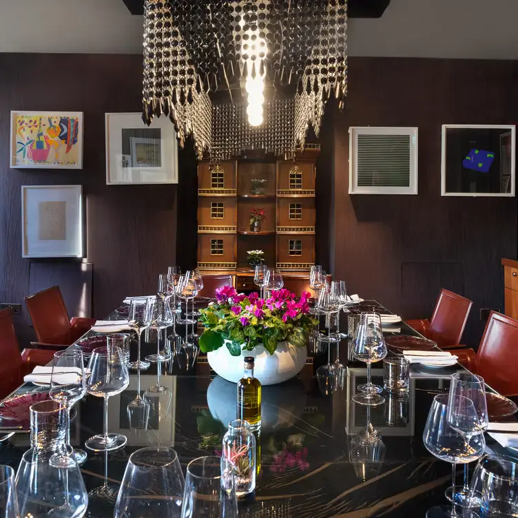 A long table at Pied A Terre with framed pictures on the wall behind it and an ornate lighting fixture hanging above it.