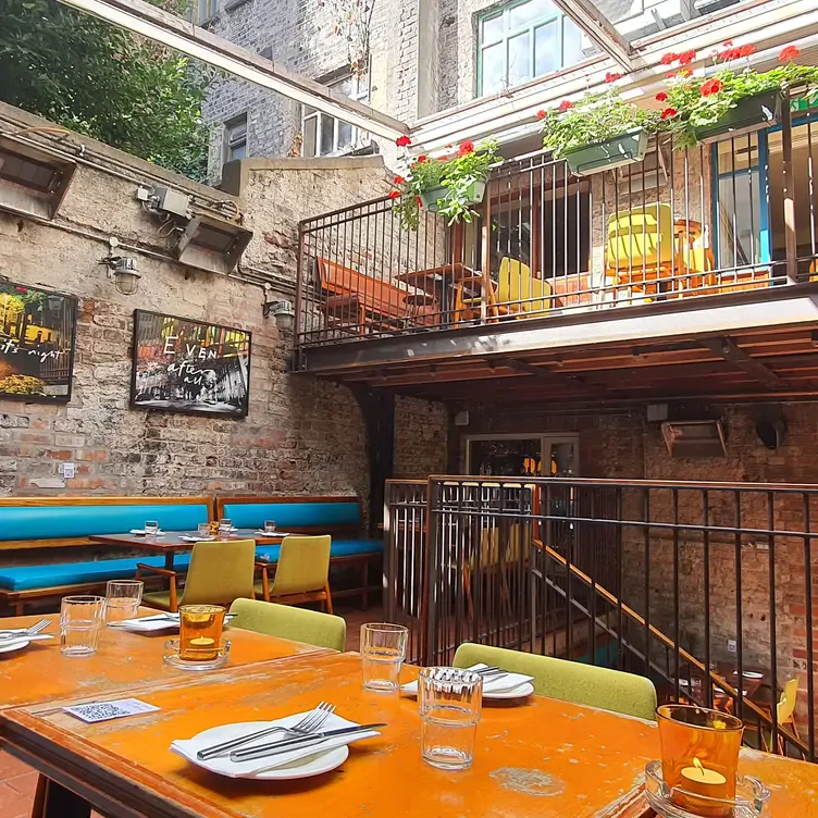 The sheltered outdoor dining space at Dury Buildings, with wooden tables and blue and green chairs.