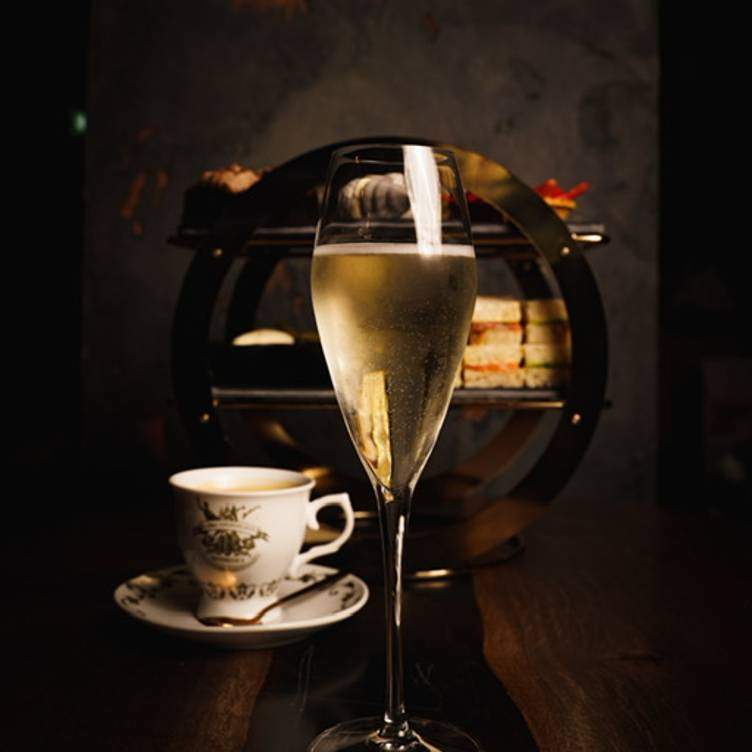 A glass of champagne sits in front of a cup of tea and sandwiches at Moskito, one of the best brunch restaurants in Glasgow.