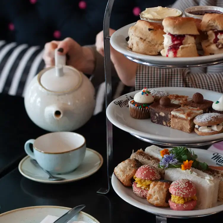 A table of afternoon tea cakes, scones and sandwiches with a diner pouring a cup of tea at Mimi’s Bakehouse, one of the restaurants with the best brunch in Edinburgh.