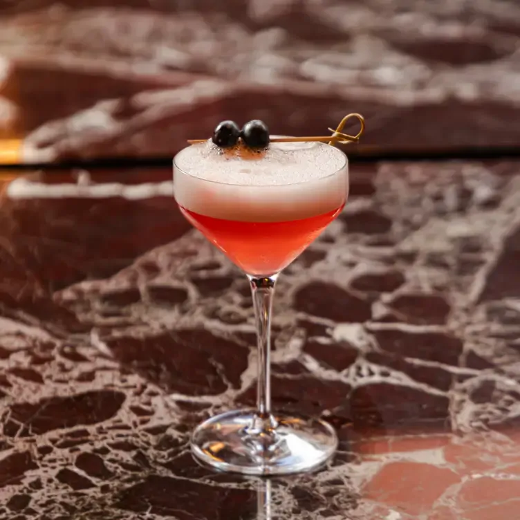 A red, pink cocktail with olives sits on the bar at Madeleine Bar, one of the best brunch restaurants in Birmingham.