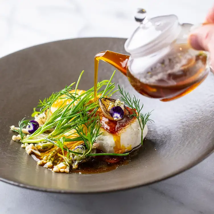 A hand pours dressing over a fish dish at Quaglino’s, one of the best live music restaurants in London.