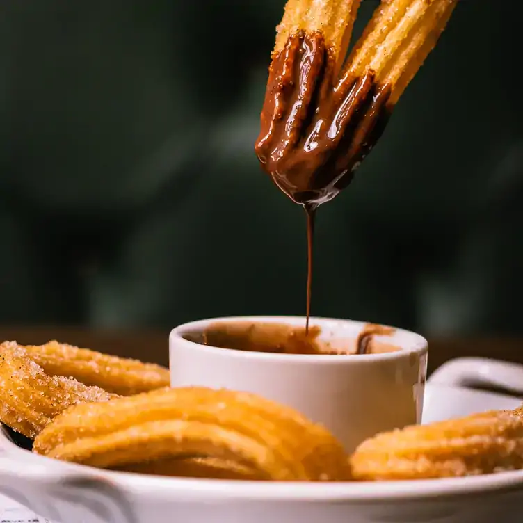 A churro being dipped into chocolate.