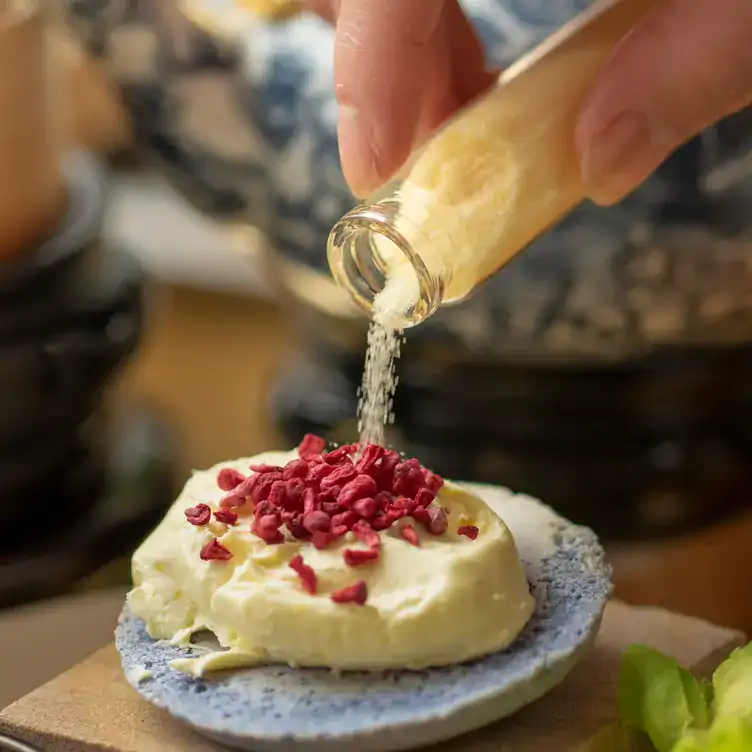 Someone pours a powdery ingredient over an a canapé topped with red granules at Kai, a Chinese MICHELIN starred restaurant in London