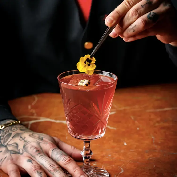 A barman tops up a red cocktails with a yellow flower at Quaglino's