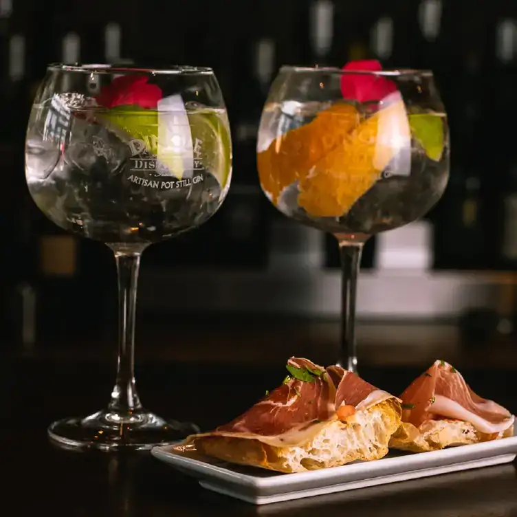 Two large cocktails with a plate of jamon on bread.