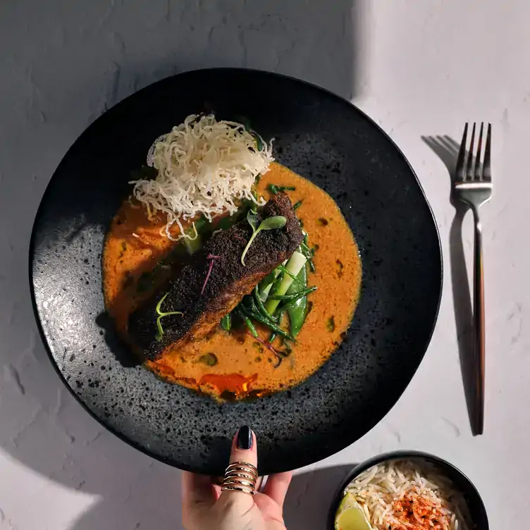 A black bowl featuring salmon in an orange sauce at The Alchemist Bar & Restaurant, one of the best restaurants in Berlin.