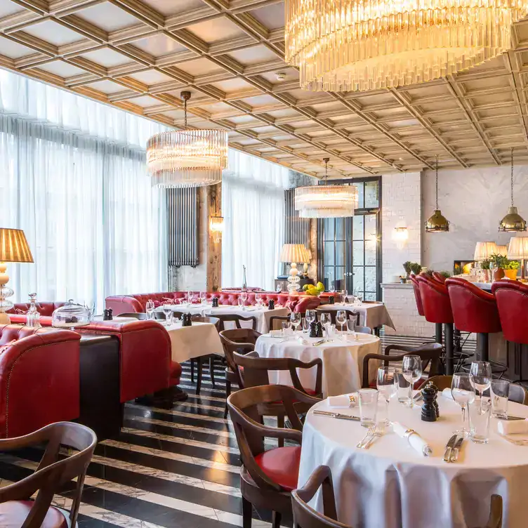 Elegant interiors with hanging chandeliers, red leather stools and white tablecloths at Cecconi‘s Berlin.