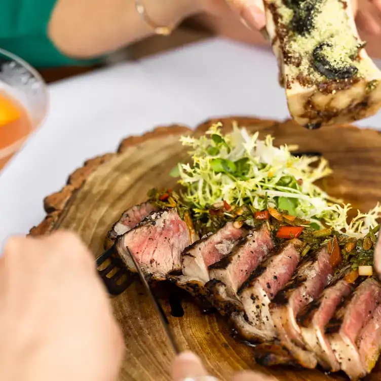 A diner cuts through a steak on a chopping board with a side salad at Butlers Wharf Chop House Restaurant, one of the best riverside restaurants in London.