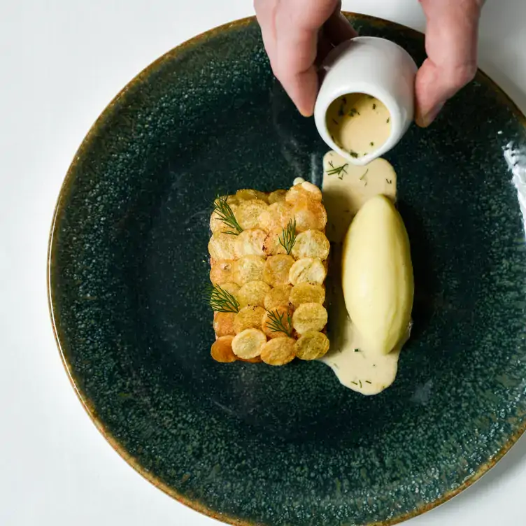 A hand pours a creamy sauce over a crispy potato dish at Myrtle, in Chelsea.