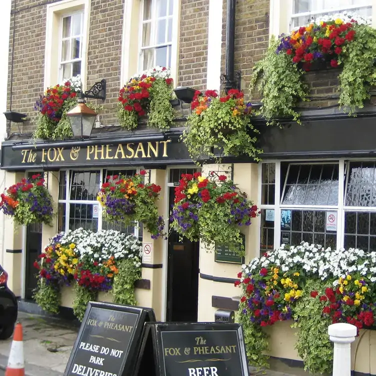 The exterior view of the pub’s façade with flowers hanging from the windowsills at The Fox & Pheasant, one of the best restaurants in Chelsea, London.