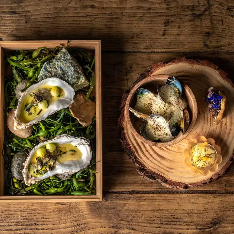 A dish of oysters on a bed of green beans and a dish of mussels served on top of a plate that looks like a tree trunk at Ekstedt at the Yard.