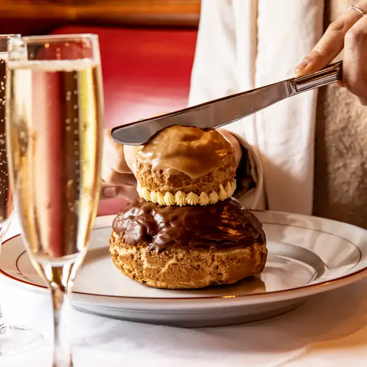 A diner cuts into a dessert with two profiteroles stacked on top of each other served alongside a flute of sparkling wine at Au Pied de Cochon.