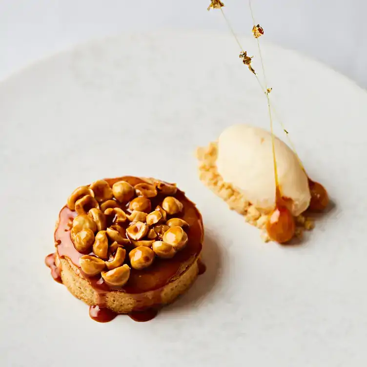 A dessert tart topped with hazelnuts and a scoop of ice cream on the side at Francatelli in London