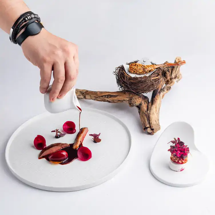 Someone pours a red sauce over a meat dish garnished with flowers served at SOLA SOHO, which has one of the best tasting menus in London.