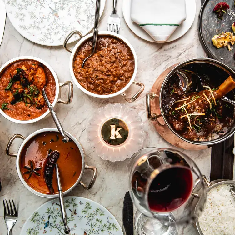 A table of various curry dishes and a glass of red wine at Kutir, in Chelsea.