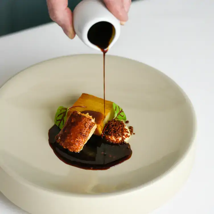 A hand pours a dark over a main dish, at Myrtle, in Chelsea.