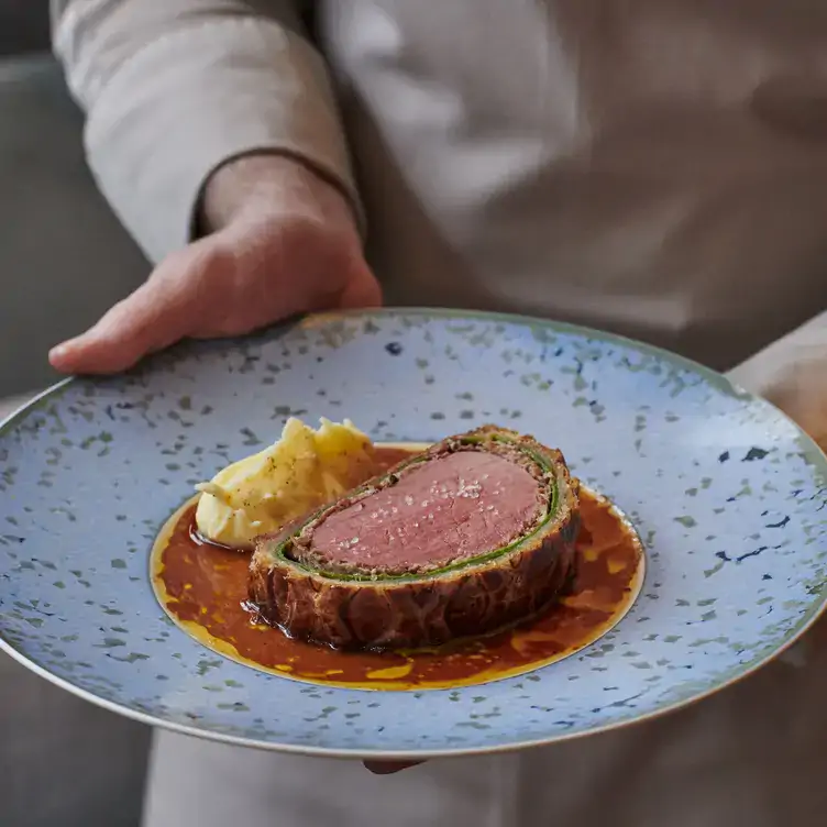 Someone carries a plate with a slice of beef wellington served on top of a brown sauce at Pavyllon, which has one of the best tasting menus in London.