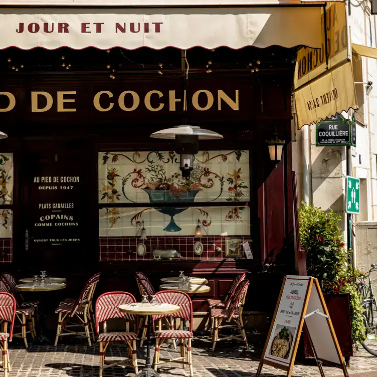 The exterior of Au Pied de Cochon, showing the red and white striped chairs and artwork in the windows.