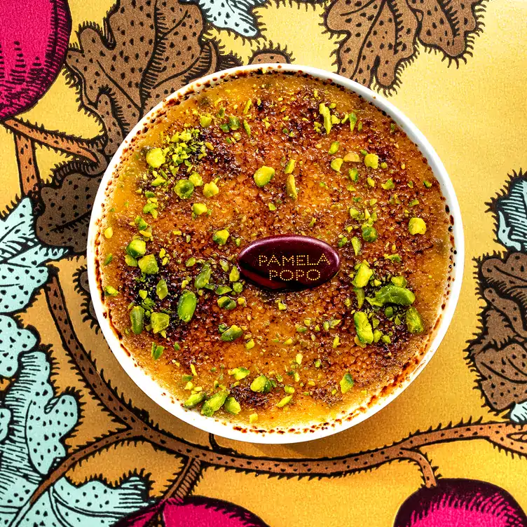 A creme brulée topped with pistachio served on a colourful, leafy table at Pamela Popo, one of Paris’ best restaurants.