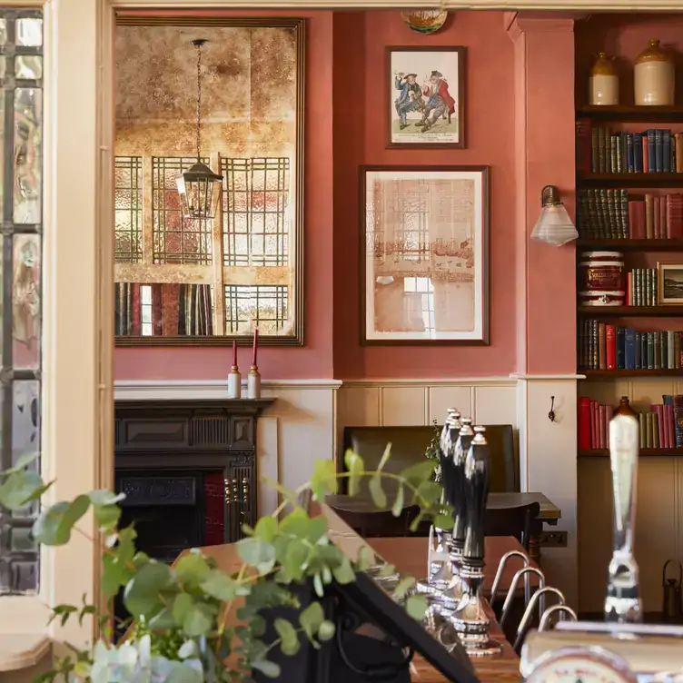 The classic pub interior with art on the walls and books on the shelves at The Surprise Chelsea, one of the best restaurants in Chelsea, London.