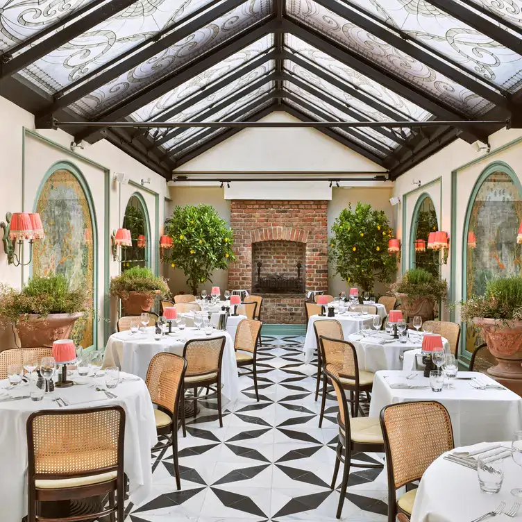 The elegant conservatory and dining room with ornate glass roof and rustic brick fire place at Daphne’s, one of the best restaurants in Chelsea, London.