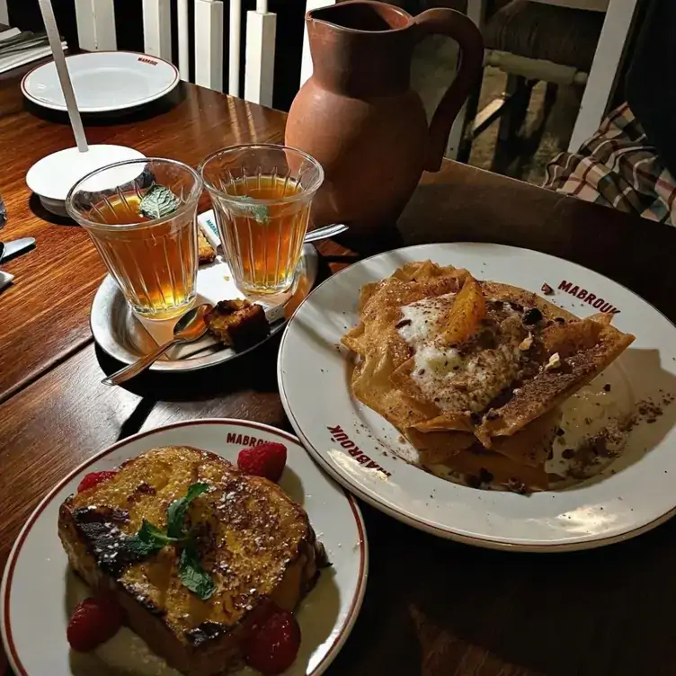 A table with desserts including fried Tunisian toast served alongside drinks from a terracotta-style jug at Mabrouk, one of the best restaurants in Paris.