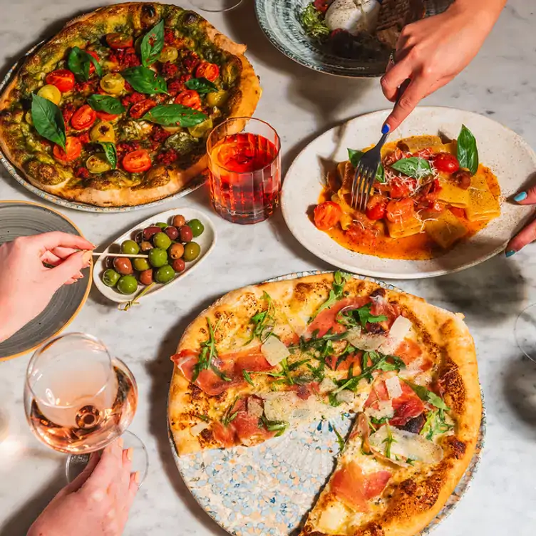 Pizzas and pasta dishes with olives on a table at Riva Italian, one of the best restaurants in Birmingham.