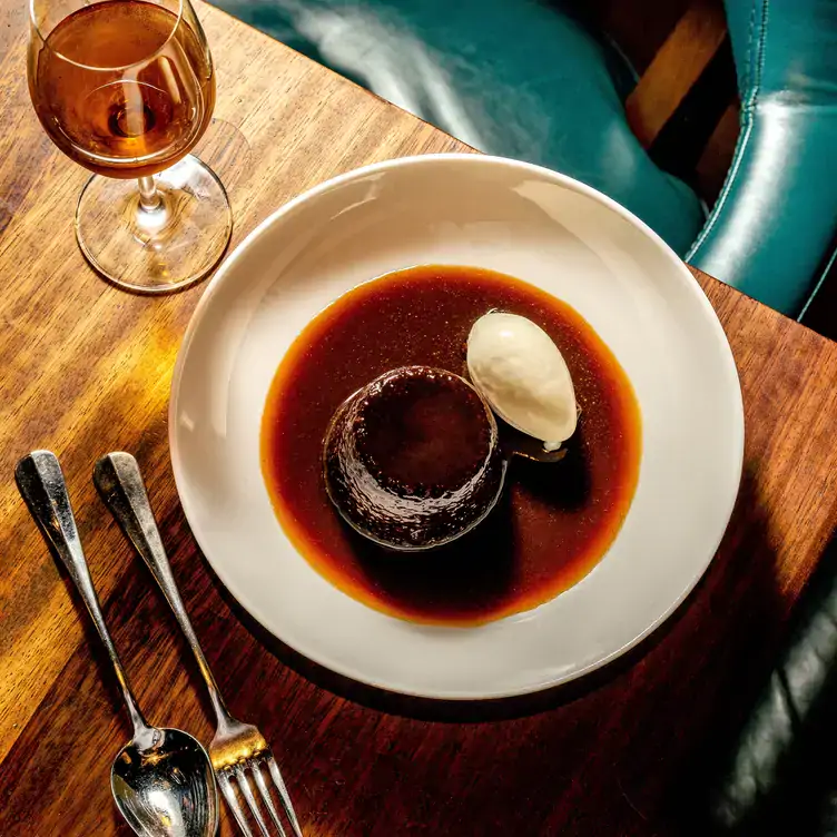 Warm dessert served with sauce and a side of ice cream with a glass of brandy on the side at Hawksmoor Manchester.