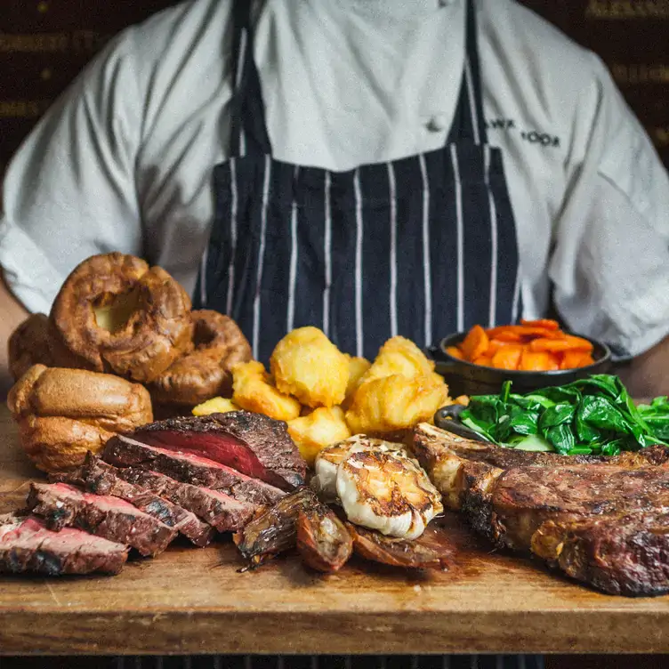 A chef holds a board with steak, roast beef, Yorkshire puddings and potatoes at Hawksmoor Manchester.