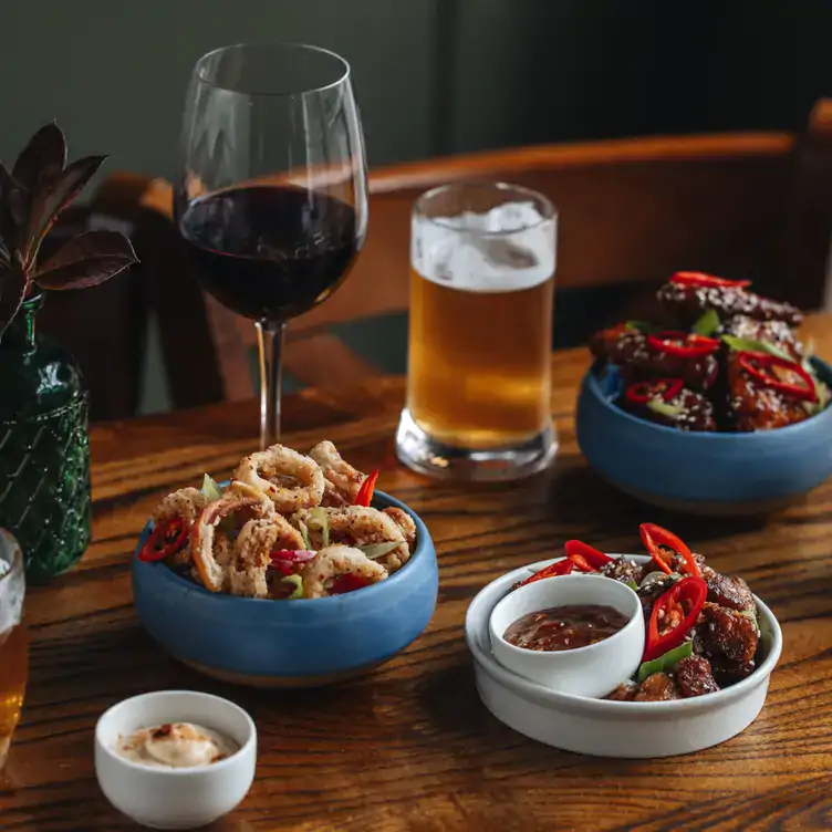 A glass of wine and pint of lager on a pub table surrounded by bar snacks, at The Barony Bar, one of the best pubs in Edinburgh.