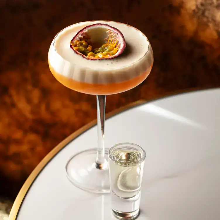 A foamy cocktail garnished with passionfruit and served alongside a shot at Amici Lounge, one of the best bars in Soho.