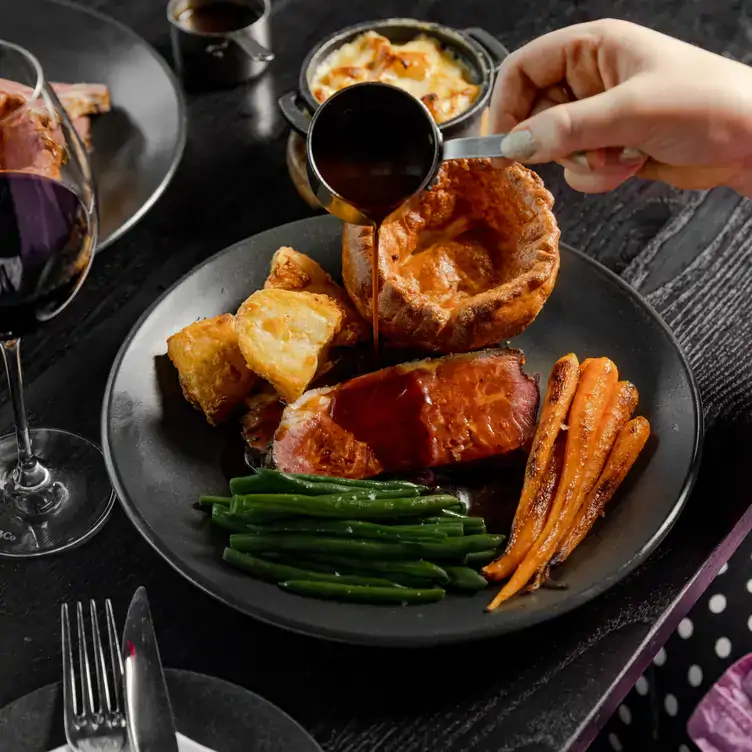 Diner pouring gravy from a jug onto a Sunday dinner at Gaucho, one of the best spots for Sunday roasts in Edinburgh.