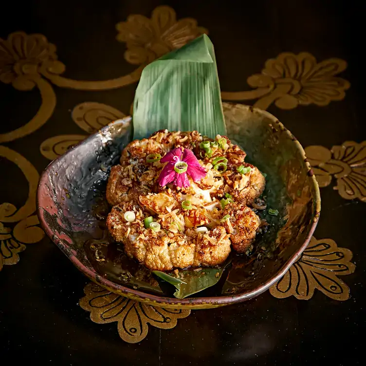 A dish served on a large leaf garnished with a pink flower at Gilgamesh Covent Garden, one of the best restaurants in Covent Garden.