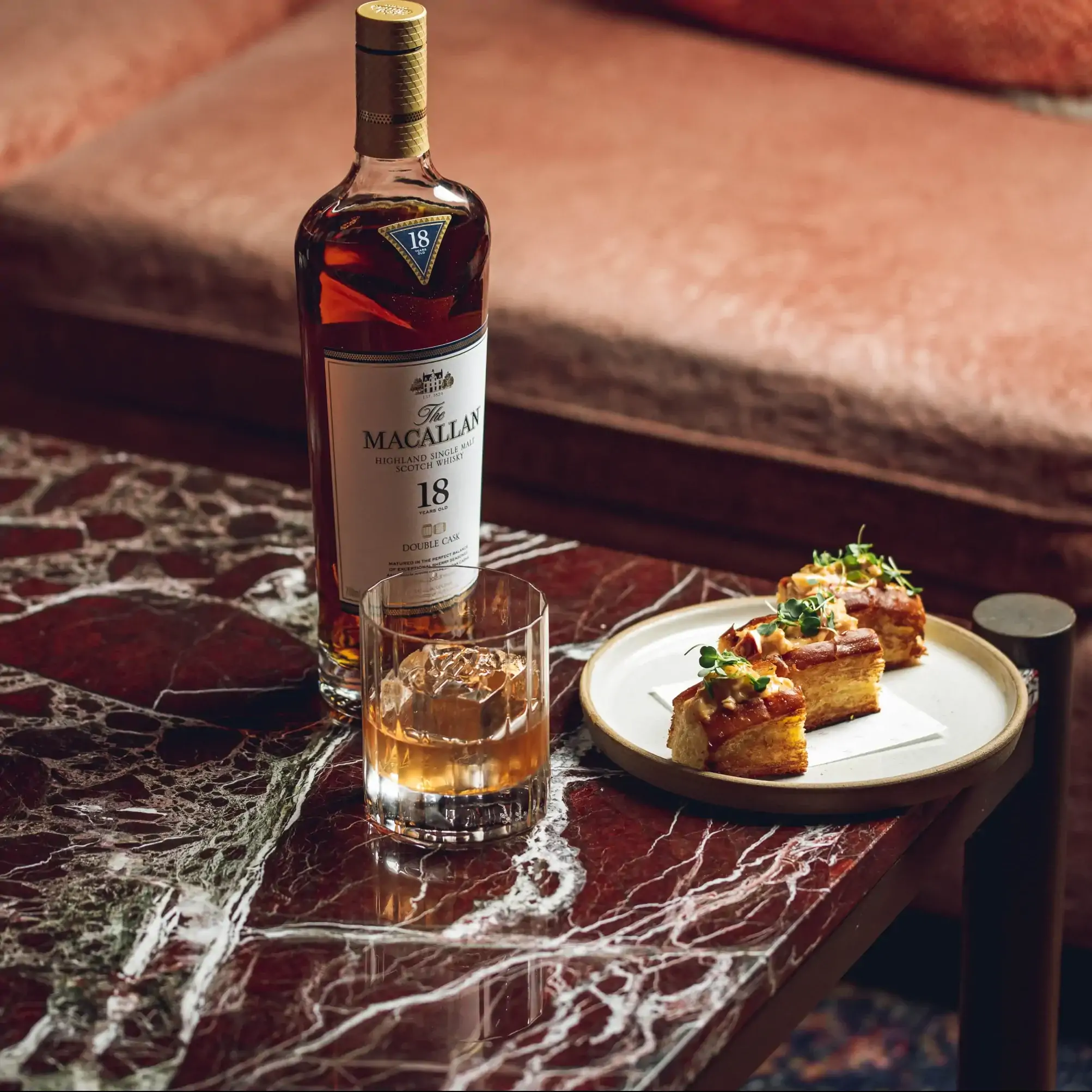 A bottle of Macallan whisky with a glass and a plate of snacks on a table at Madeleine Bar at The Grand Hotel, one of the best restaurants for Christmas dinner.