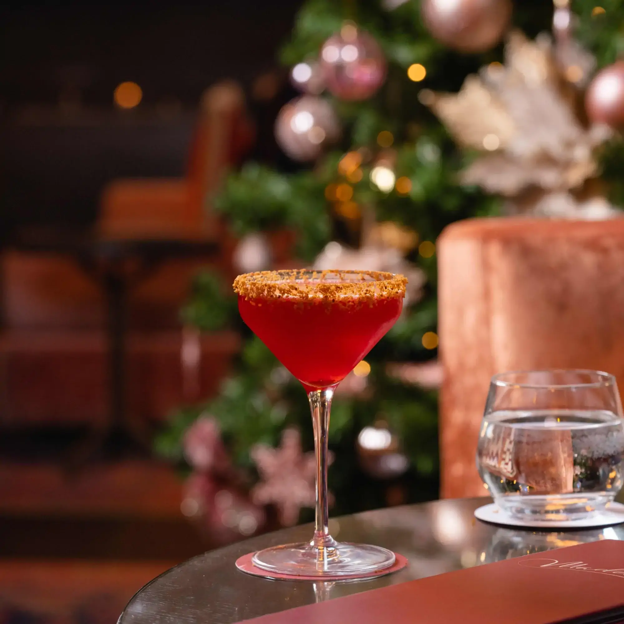 A red cocktail on a table at Madeleine Bar at The Grand Hotel, one of the best Christmas dinner restaurants in the UK, with a Christmas tree in the background.