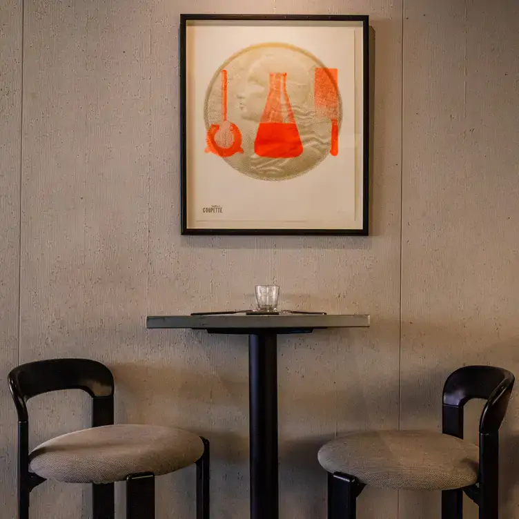 A table with two seats against an industrial grey wall with a frame at Atelier Coupette in Soho, one of the best bars for Dry January in London