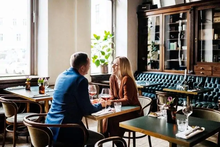 A couple sitting at a restaurant table smiling at each other and holding hands over a dining table with two glasses of wine