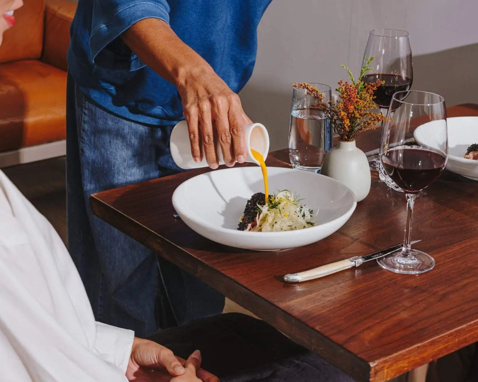 A waiter pouring sauce in the dish of a diner at a restaurant